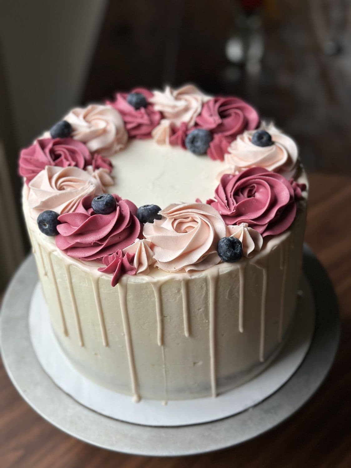 A white drip cake with blush buttercream roses and blueberries