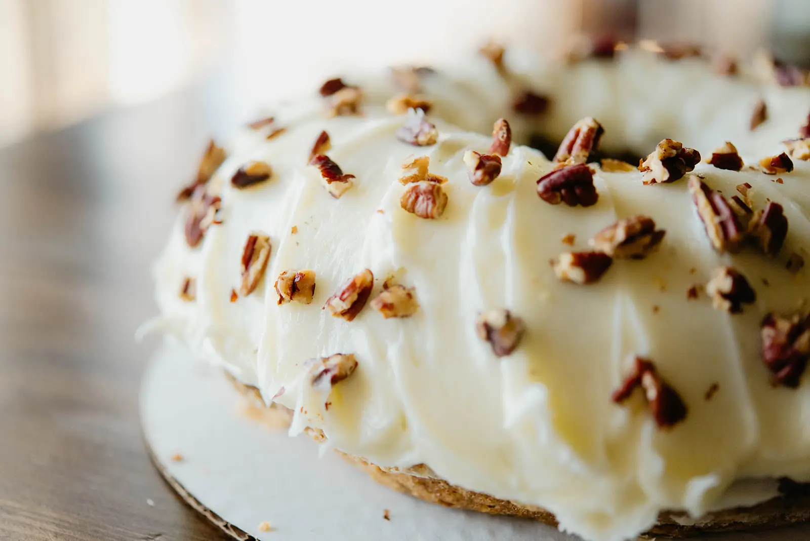 Close detail of a cream-cheese-frosted bundt cake with chopped pecans