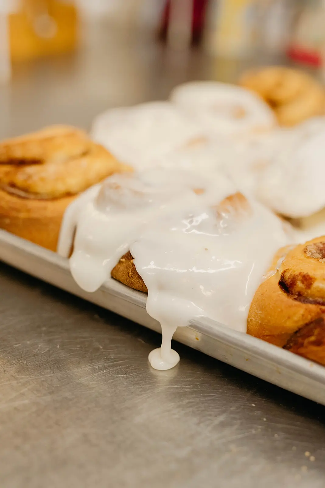 Fresh cinnamon rolls on a baking tray with icing dripping over the edge