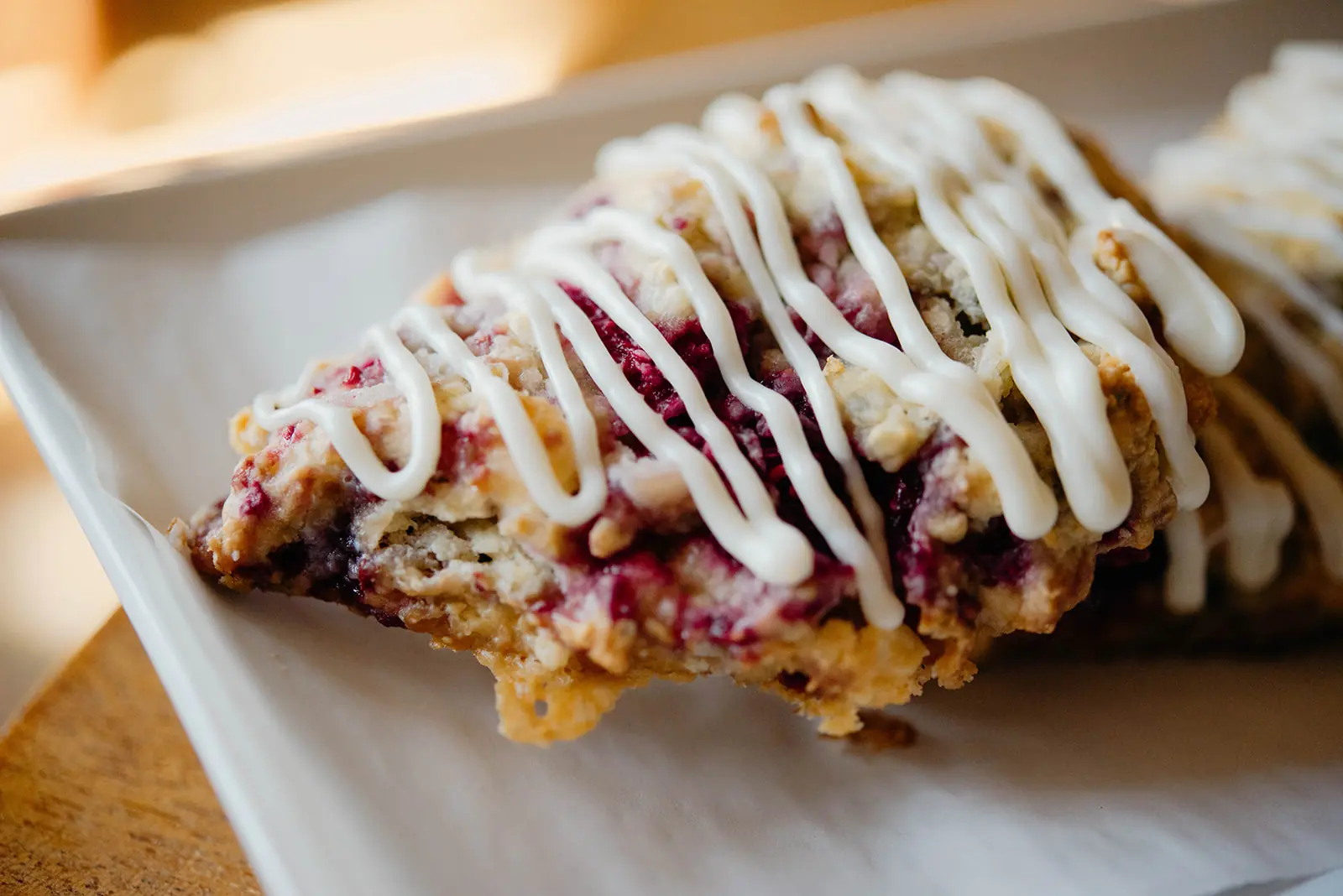 A glazed berry scone with drizzled icing on parchment