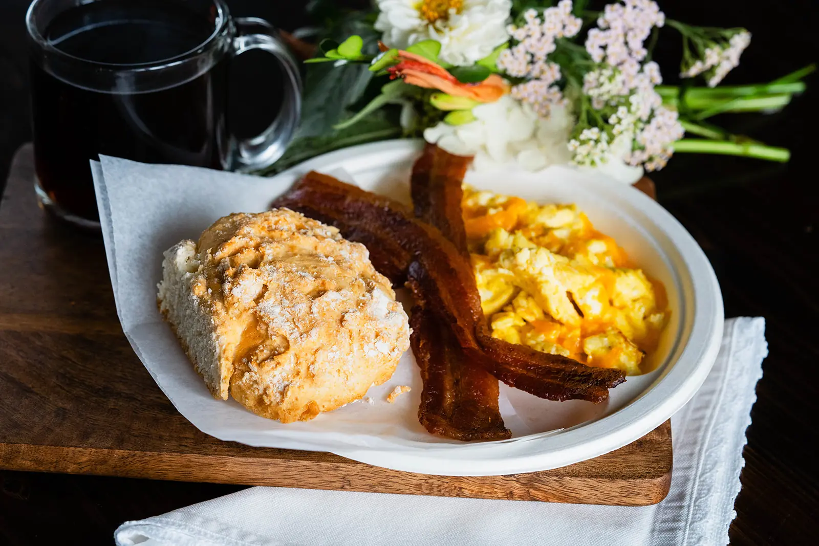 A breakfast plate with a biscuit, bacon, and cheesy scrambled eggs