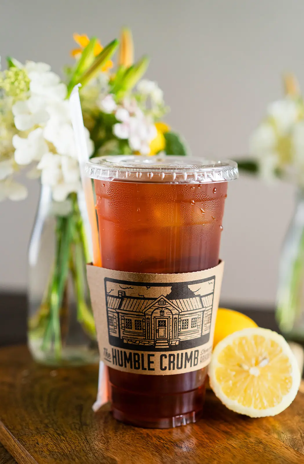Iced tea in a to-go cup with a kraft Humble Crumb sleeve and a halved lemon