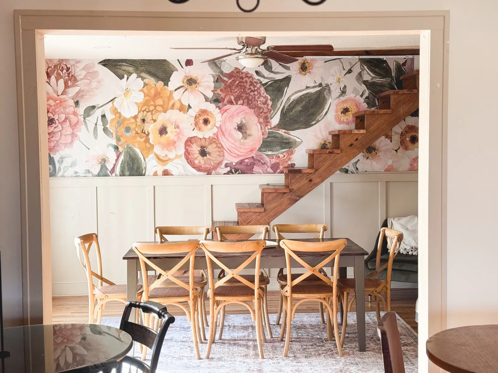 The Christiana Room through a doorway, with a floral mural, wooden stairs, and a dining table on a patterned rug
