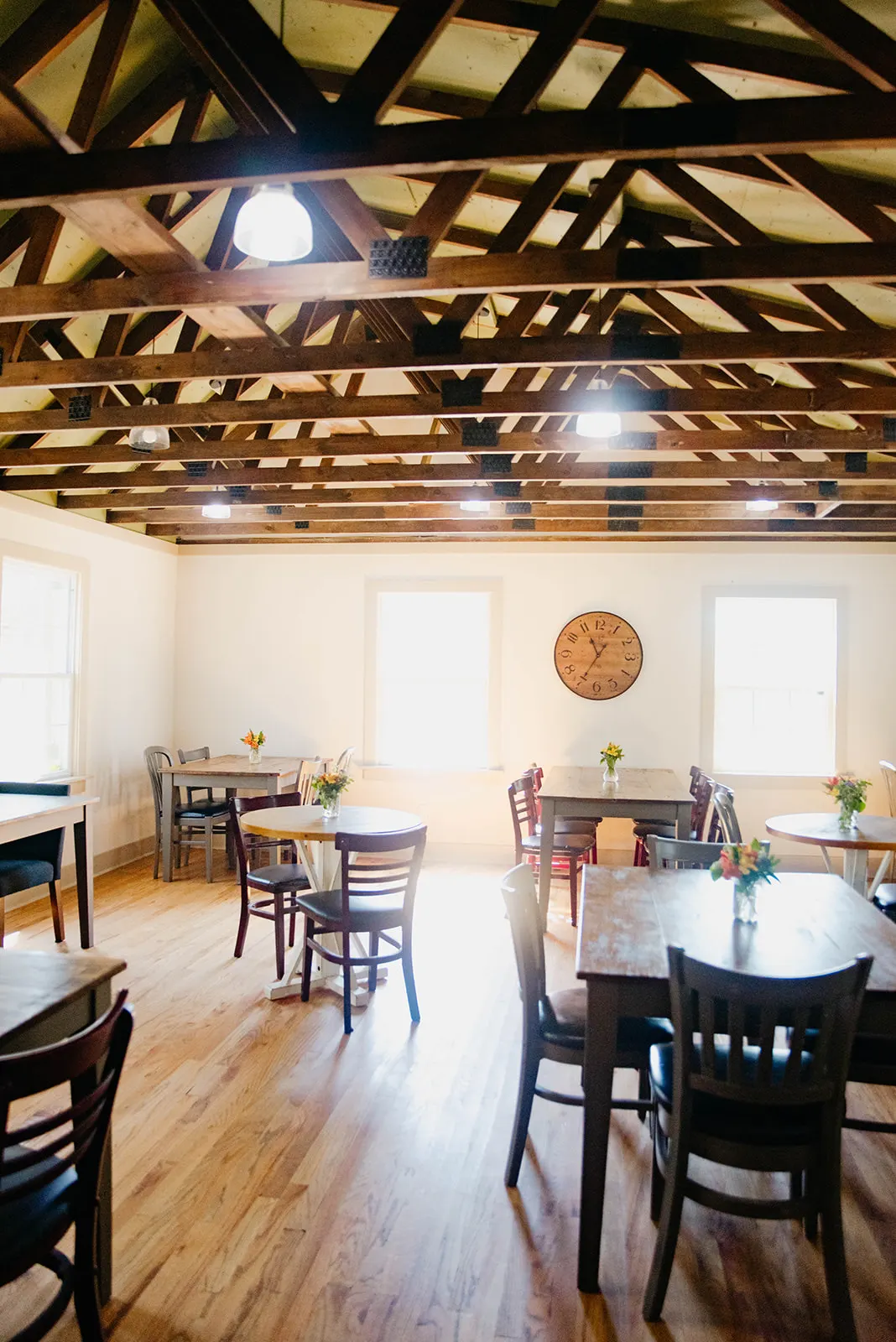 The Kellogg Room with wooden tables, a round wall clock, and bright windows under exposed beams